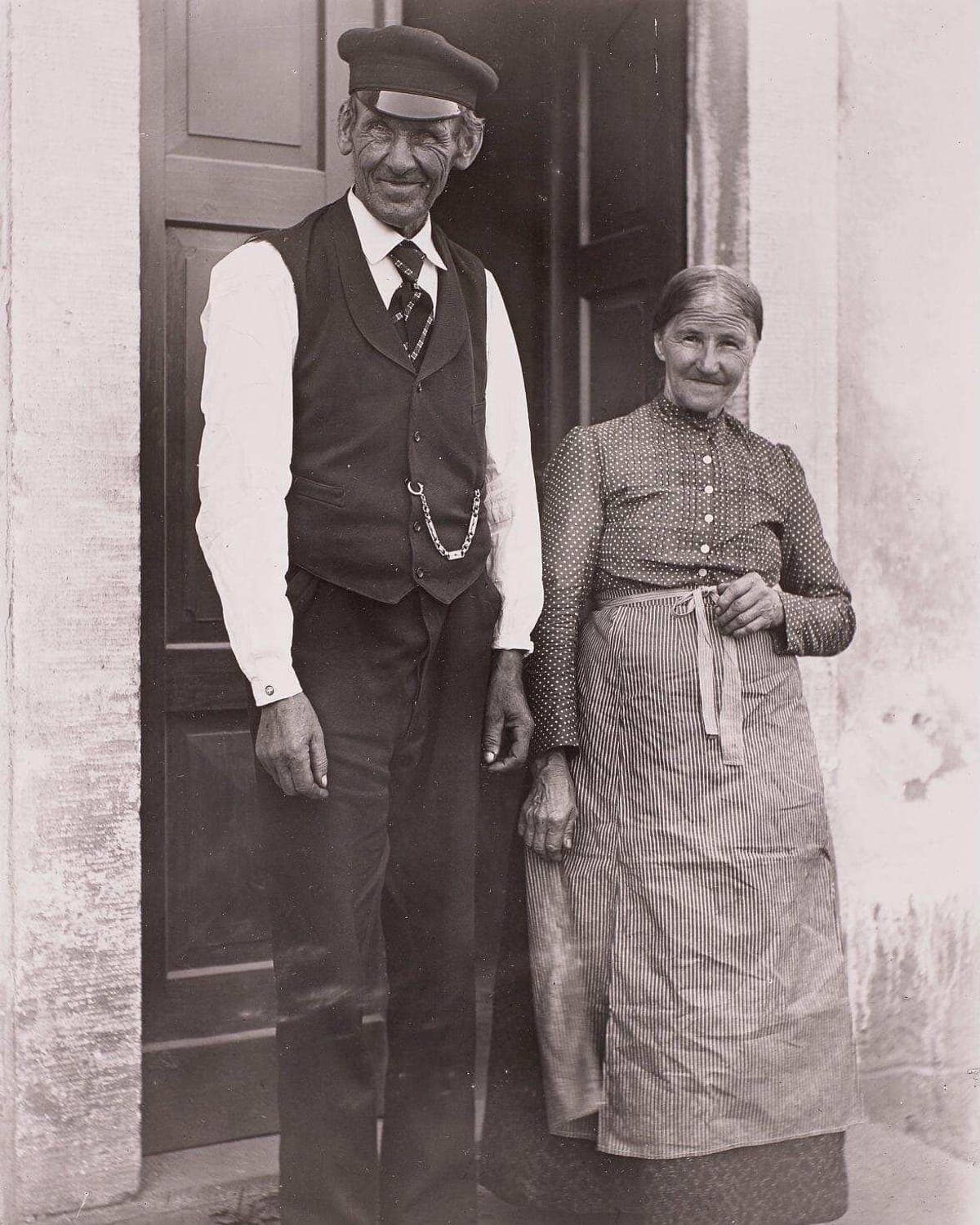 Altes Ehepaar vor seiner Haustür, Eschdorf um 1904: links das Original in Sepia mit Flecken, rechts mit KI restauriert und koloriert.